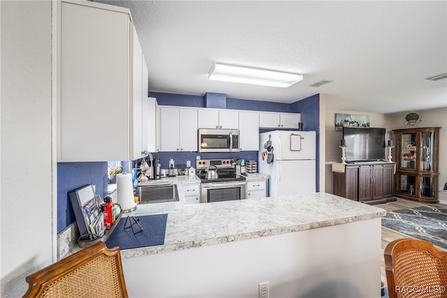 kitchen with white cabinets, sink, appliances with stainless steel finishes, light hardwood / wood-style floors, and kitchen peninsula