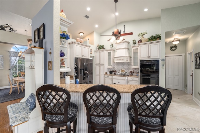 kitchen with light stone countertops, double oven, kitchen peninsula, lofted ceiling, and custom exhaust hood