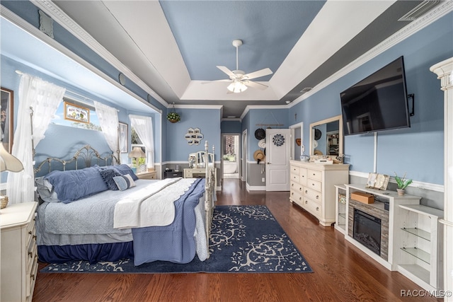 bedroom featuring ornamental molding, a tray ceiling, ceiling fan, and dark wood-type flooring