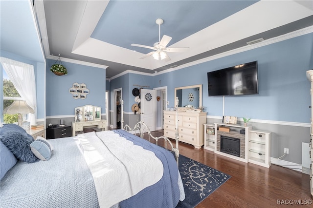 bedroom featuring ceiling fan, a raised ceiling, a stone fireplace, dark hardwood / wood-style flooring, and ornamental molding