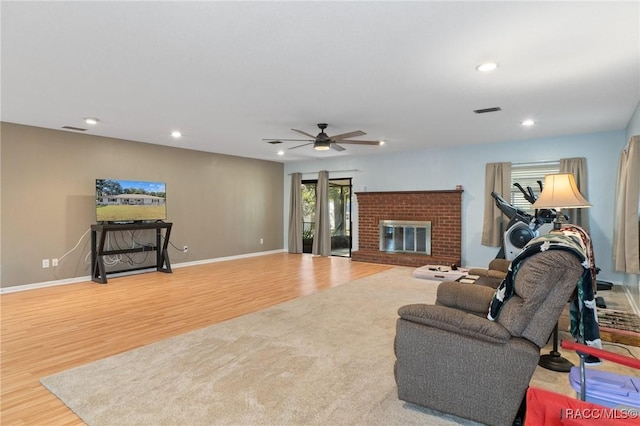 living room featuring light hardwood / wood-style floors, a brick fireplace, and ceiling fan