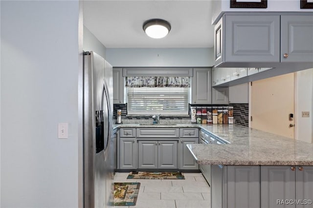 kitchen featuring gray cabinetry, sink, stainless steel fridge with ice dispenser, light stone counters, and kitchen peninsula