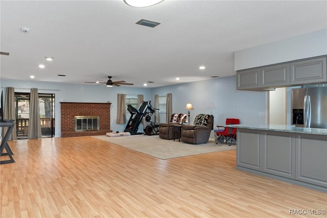 workout area featuring a brick fireplace, ceiling fan, and light hardwood / wood-style flooring