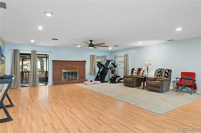 exercise room featuring ceiling fan, light hardwood / wood-style floors, and a brick fireplace