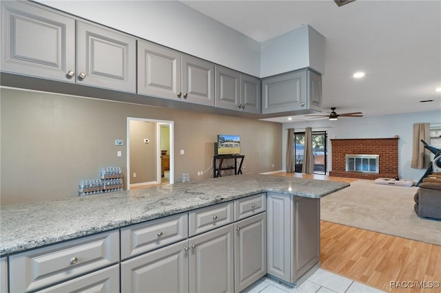 kitchen with ceiling fan, light stone countertops, light hardwood / wood-style flooring, kitchen peninsula, and a fireplace