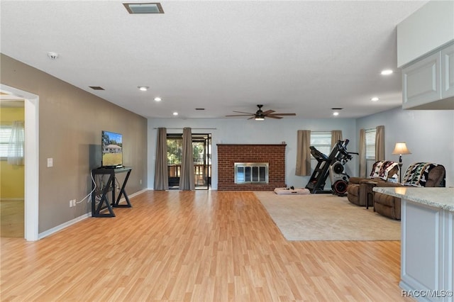 living room featuring ceiling fan, light wood-type flooring, and a brick fireplace