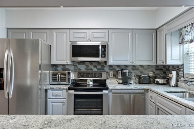 kitchen with stainless steel appliances, light stone counters, tasteful backsplash, and sink