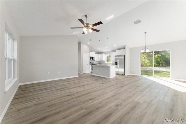 9065 N Arcadia Way, Citrus Springs, FL 34434 - unfurnished living room featuring ceiling fan with notable chandelier, visible vents, vaulted ceiling, light wood-style flooring, and baseboards