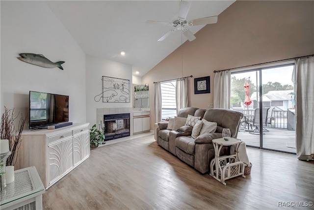 living room featuring a tiled fireplace, a wealth of natural light, high vaulted ceiling, and light hardwood / wood-style floors