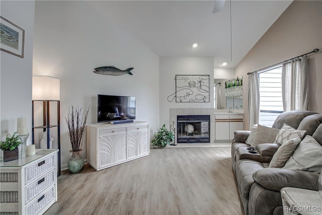 living room with a tile fireplace, high vaulted ceiling, and light wood-type flooring