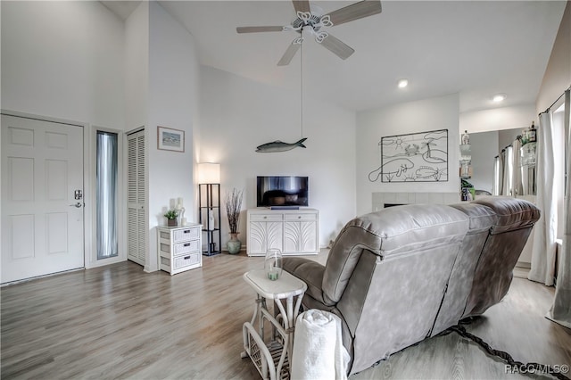 living room with a tiled fireplace, ceiling fan, high vaulted ceiling, and light hardwood / wood-style floors