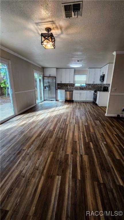 unfurnished living room with a textured ceiling, dark hardwood / wood-style floors, and ornamental molding