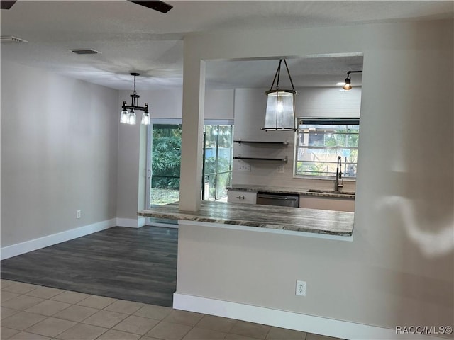 kitchen with decorative light fixtures, dark countertops, white cabinetry, a sink, and dishwasher