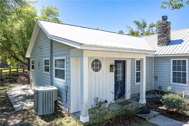 exterior space featuring a standing seam roof, metal roof, central AC, fence, and a chimney