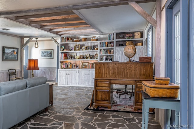 sitting room with built in shelves, visible vents, wainscoting, stone floors, and beamed ceiling