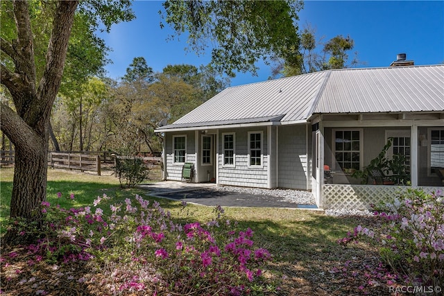 rear view of house featuring metal roof, a patio, fence, a lawn, and a chimney