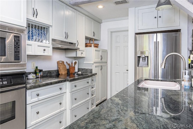 kitchen with white cabinets, under cabinet range hood, dark stone counters, and stainless steel appliances