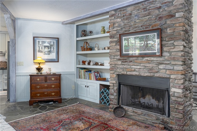 living room featuring built in features, a fireplace, stone finish flooring, wainscoting, and a textured ceiling