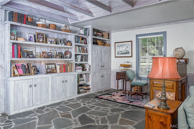 sitting room with a wainscoted wall, stone flooring, and beam ceiling