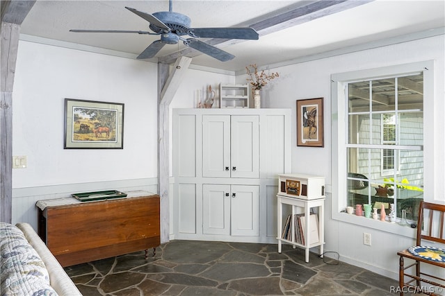 sitting room with a ceiling fan, stone floors, and a wainscoted wall