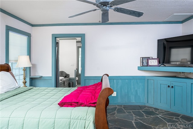 bedroom featuring visible vents, a ceiling fan, a wainscoted wall, a textured ceiling, and stone tile flooring