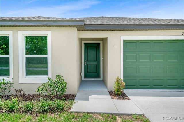 784 E Alaska Ln, Hernando, FL 34442 - view of exterior entry featuring stucco siding, a shingled roof, a garage, and driveway