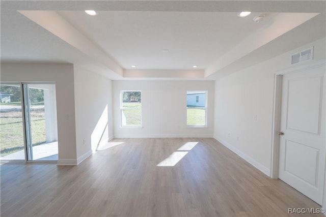 unfurnished room with light wood finished floors, a wealth of natural light, a raised ceiling, and visible vents