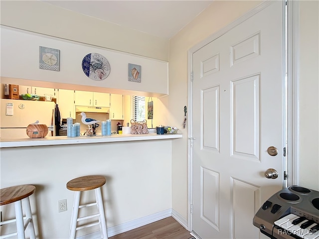 kitchen with wood-type flooring, white refrigerator, and a kitchen breakfast bar