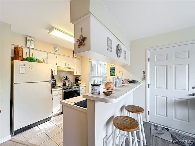 kitchen with light tile patterned flooring, gas range oven, white fridge, a kitchen bar, and kitchen peninsula