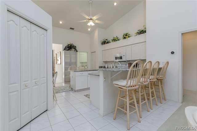 kitchen with white cabinetry, light stone countertops, high vaulted ceiling, a kitchen bar, and light tile patterned flooring