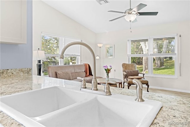 interior space with ceiling fan, light stone countertops, sink, and white cabinets