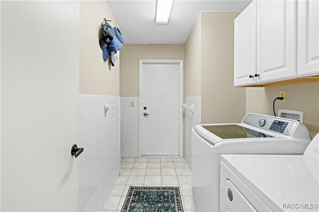 clothes washing area featuring tile walls, light tile patterned floors, washer and clothes dryer, and cabinets