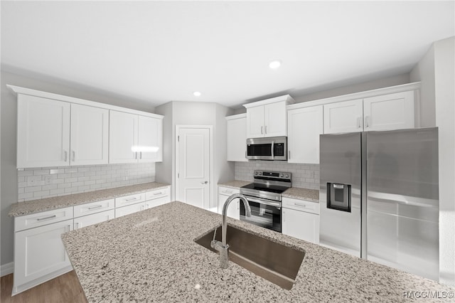 kitchen with light stone countertops, stainless steel appliances, sink, light hardwood / wood-style flooring, and white cabinets