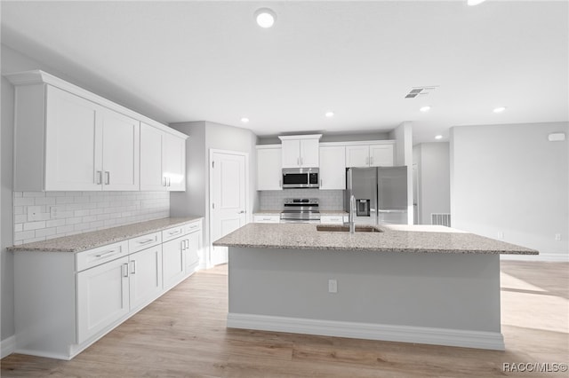 kitchen featuring white cabinetry, light hardwood / wood-style flooring, stainless steel appliances, and a center island with sink