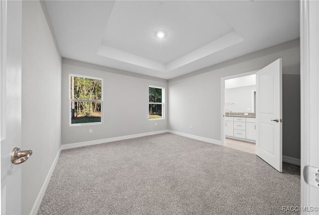 unfurnished bedroom featuring a raised ceiling, light colored carpet, and ensuite bath