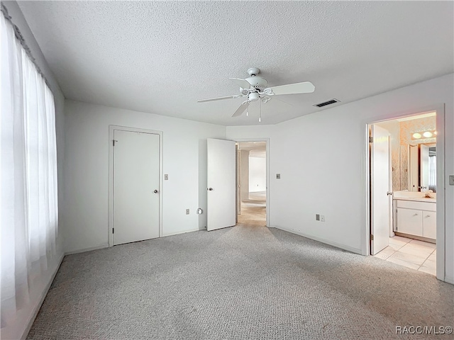 unfurnished bedroom with ceiling fan, light colored carpet, a textured ceiling, and ensuite bath