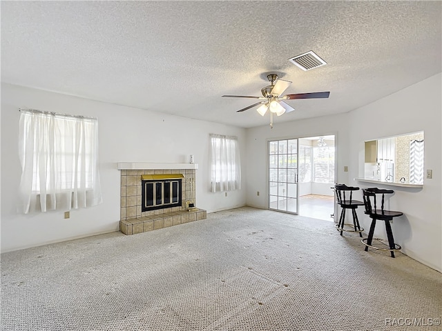 unfurnished living room with carpet flooring, ceiling fan, a fireplace, and a textured ceiling