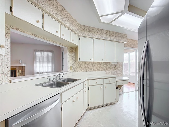 kitchen featuring kitchen peninsula, appliances with stainless steel finishes, a fireplace, sink, and white cabinets