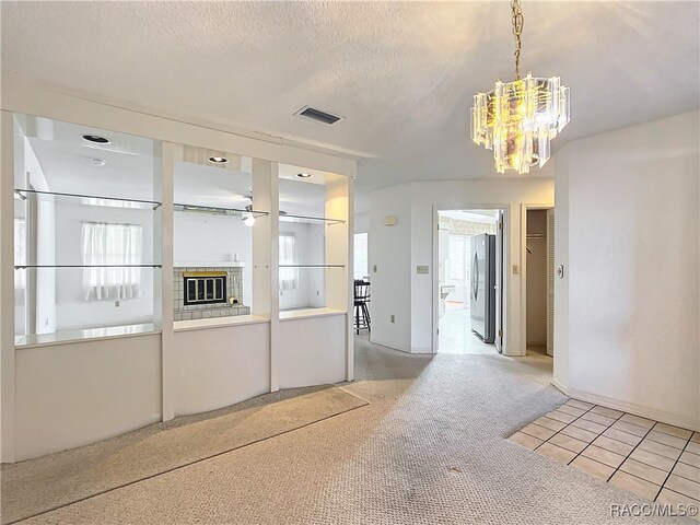 empty room featuring a chandelier, light tile patterned floors, a textured ceiling, and a tile fireplace