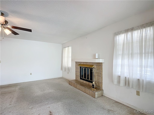 unfurnished living room featuring carpet flooring, a tile fireplace, ceiling fan, and a textured ceiling