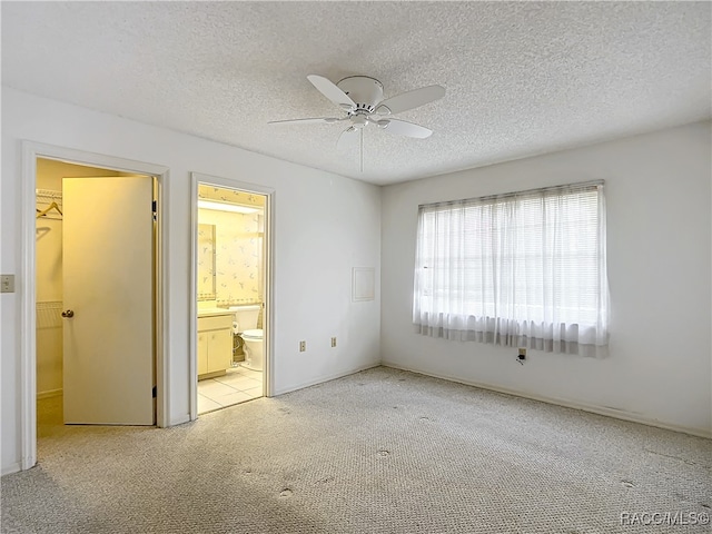 unfurnished bedroom featuring ensuite bath, a textured ceiling, light colored carpet, ceiling fan, and a closet