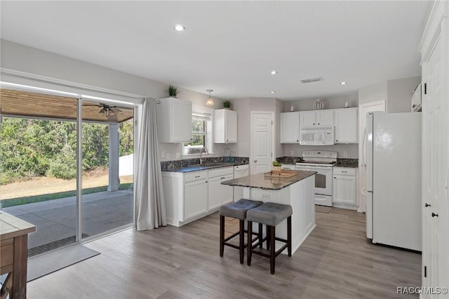 kitchen featuring a center island, wood-type flooring, white appliances, a breakfast bar, and white cabinets