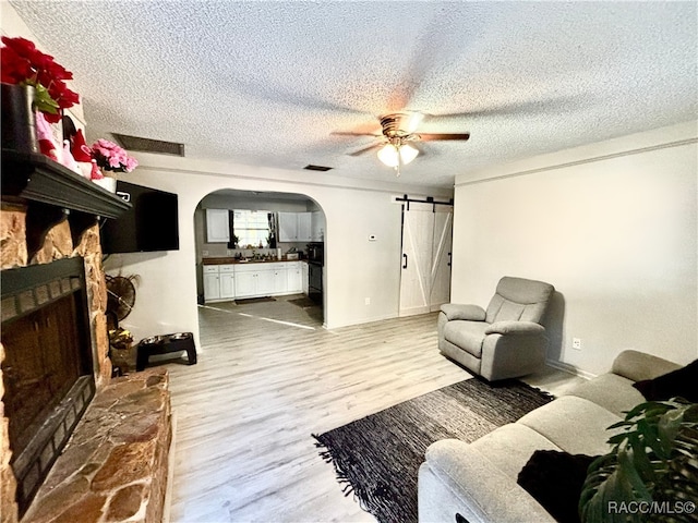 living room with ceiling fan, hardwood / wood-style floors, a textured ceiling, a stone fireplace, and a barn door