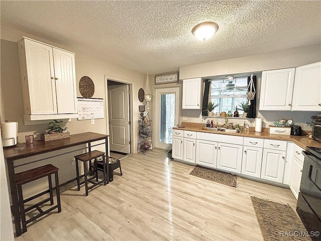 kitchen featuring sink, light hardwood / wood-style floors, white cabinets, a textured ceiling, and black range with gas stovetop