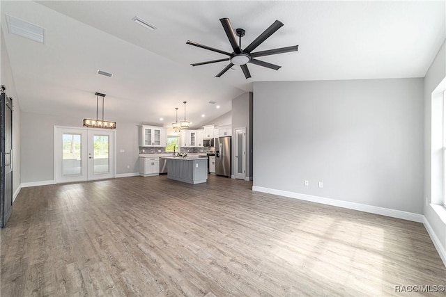 unfurnished living room featuring vaulted ceiling, a ceiling fan, wood finished floors, baseboards, and a chandelier