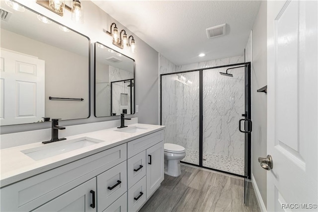 bathroom with toilet, a marble finish shower, double vanity, a textured ceiling, and recessed lighting
