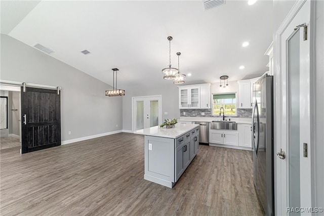 kitchen with a sink, stainless steel appliances, vaulted ceiling, wood finished floors, and a barn door