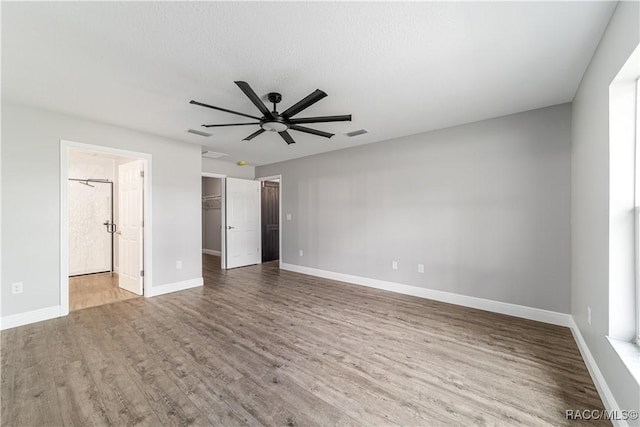 unfurnished bedroom featuring wood finished floors, baseboards, a walk in closet, ceiling fan, and ensuite bathroom
