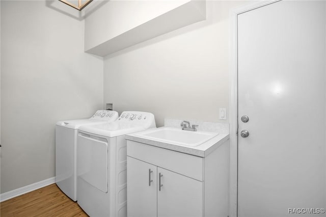 laundry room featuring baseboards, washing machine and dryer, light wood-type flooring, cabinet space, and a sink