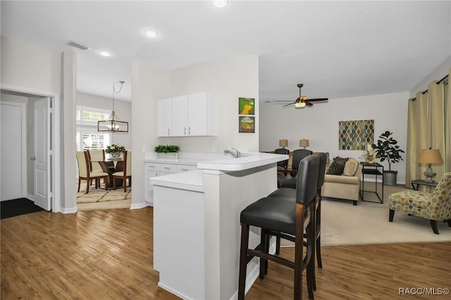 kitchen featuring visible vents, a kitchen breakfast bar, white cabinetry, a peninsula, and light countertops